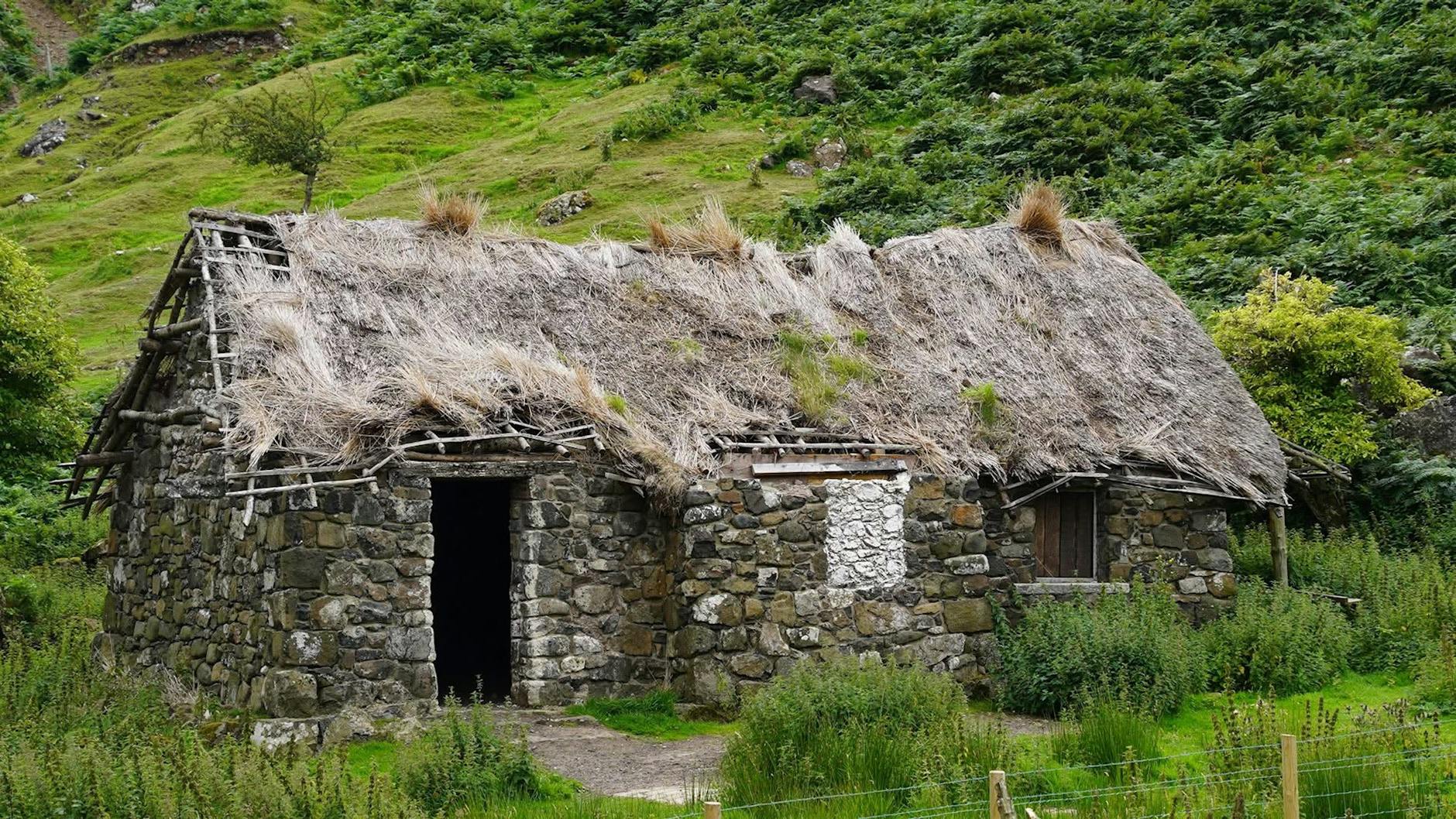 Kamienny irlandzki domek z strzechą wśród bujonej zieleni