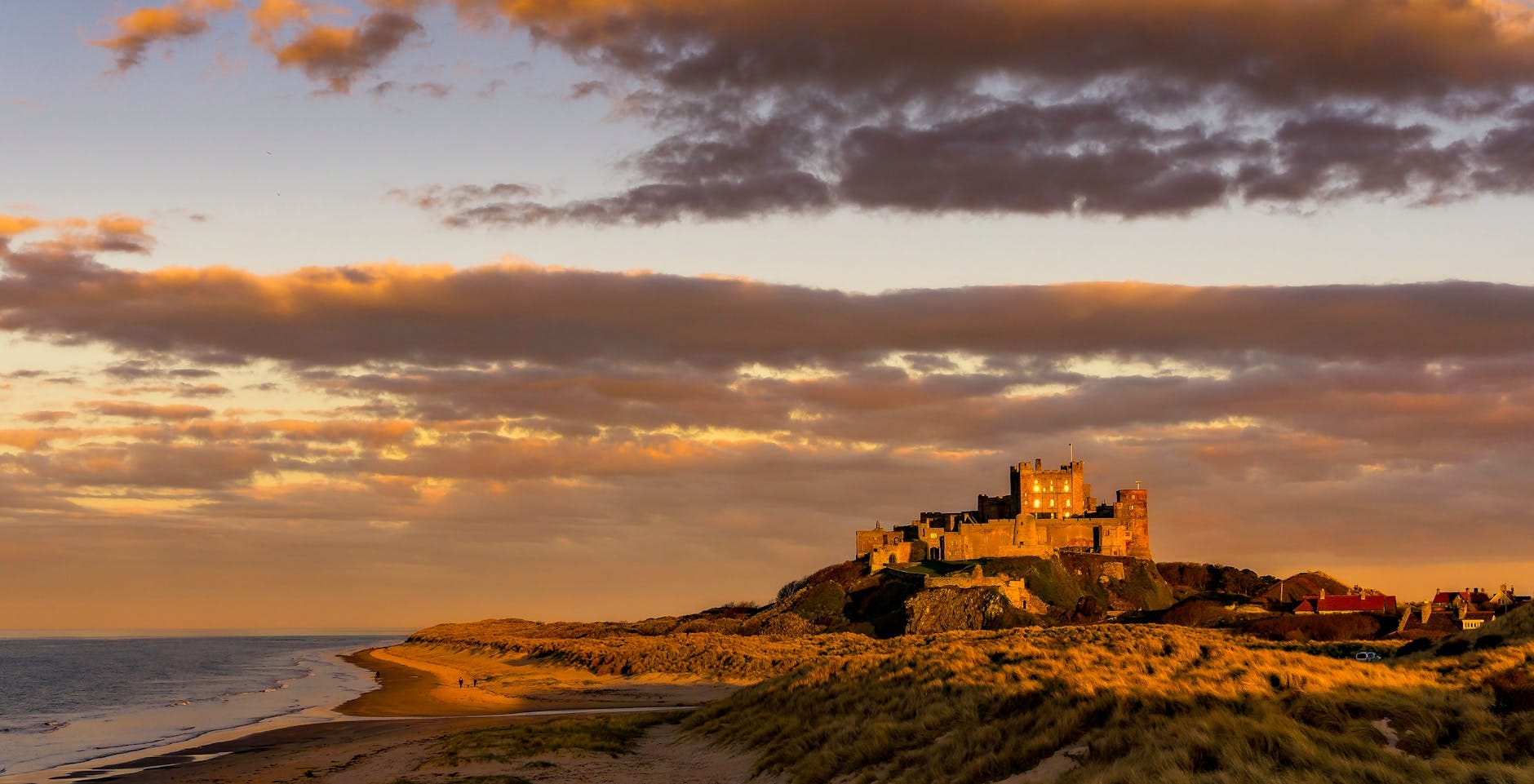 Zachód słońca nad zamkiem Bamburgh i piaszczystą plażą w Northumberland