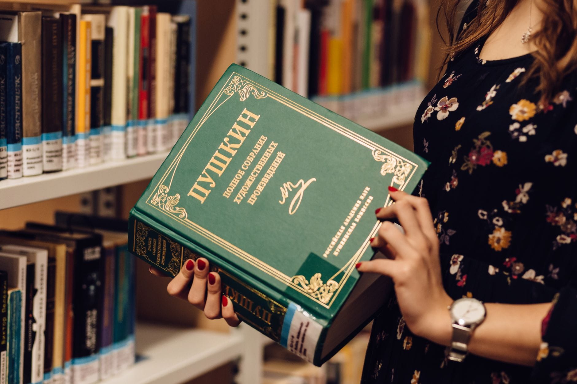 Kobieta z książką rosyjskiej literatury między regałami biblioteki