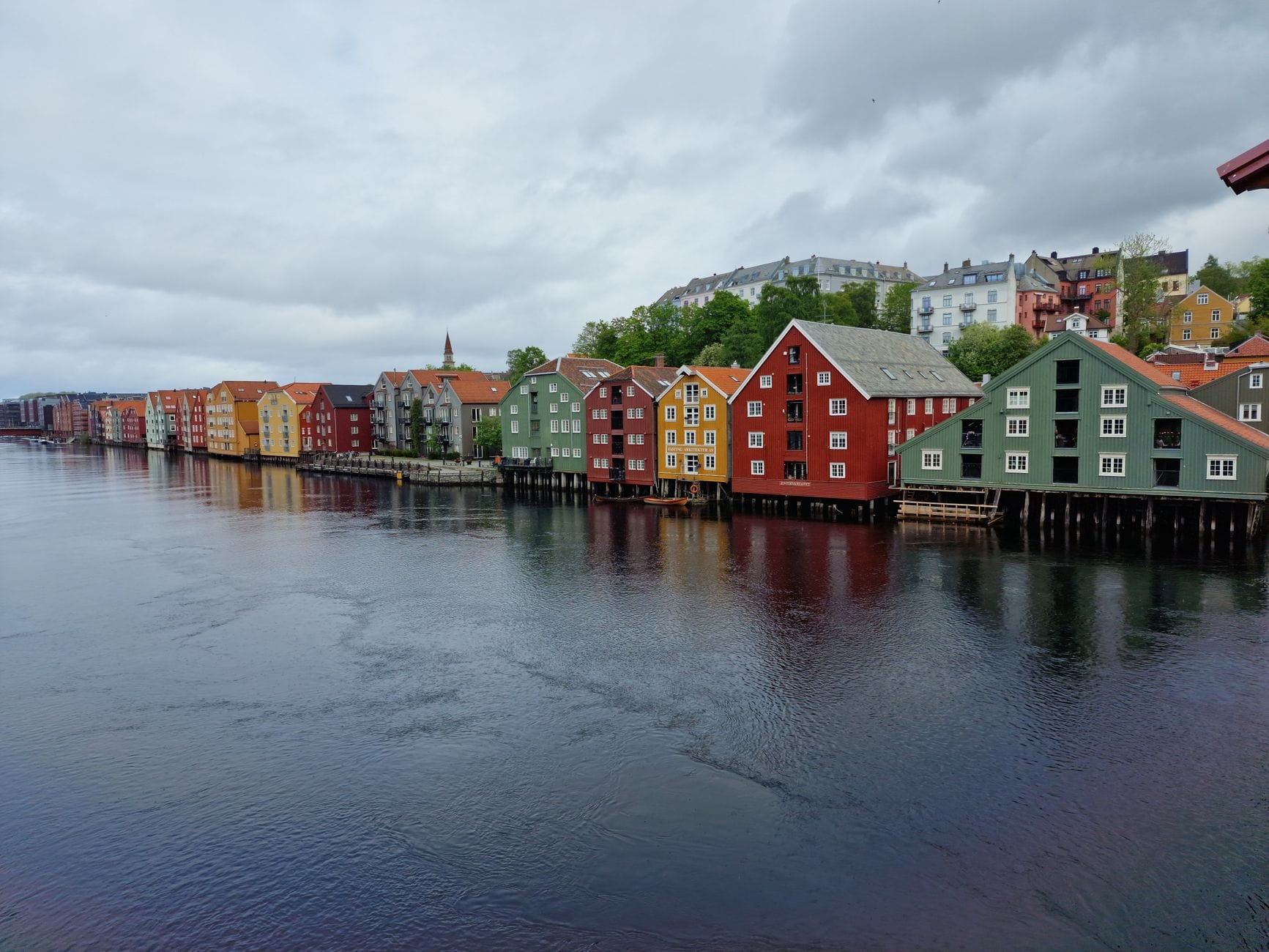 Trondheim poza przewodnikiem: drewniane zaułki, nabrzeża i lokalne kawiarnie Kolorowe drewniane domy nad wodą w Trondheim w pochmurny dzień